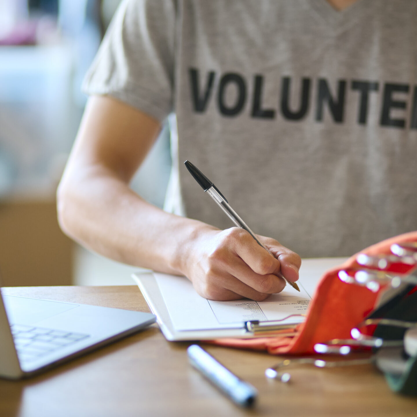 Close Up Of Male Charity Worker At Desk With Laptop Checking Clothing Donations At Thrift Store